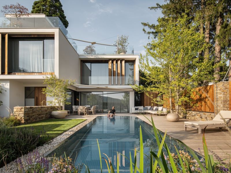 Modernes Haus mit viel Glas von Livingglas mit einer Person die am Pool sitzt 